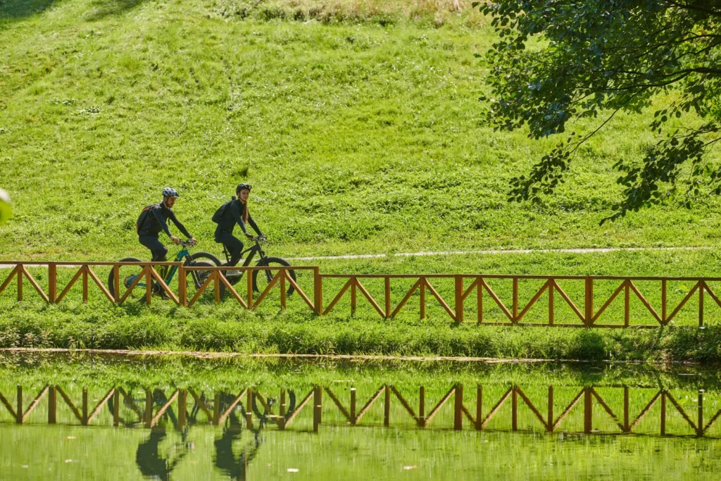 Due ciclisti in sella su una pista ciclabile a fianco di un canale con vegetazione verde rigogliosa.