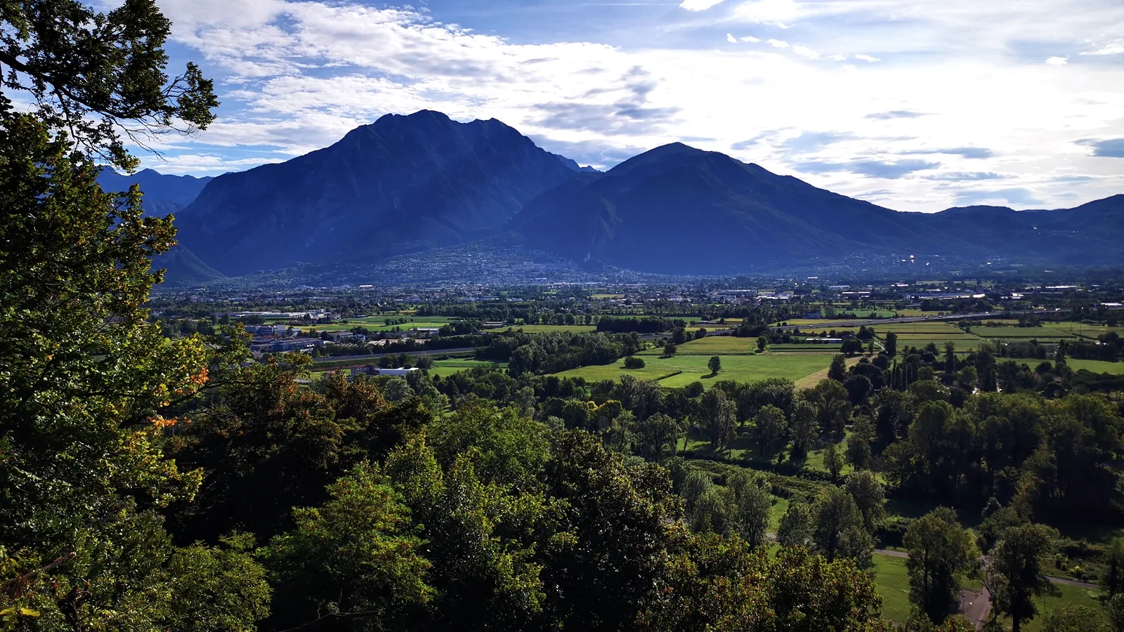 Panorama dalla collina con montagne blu sullo sfondo e verde valle coltivata a patchwork.