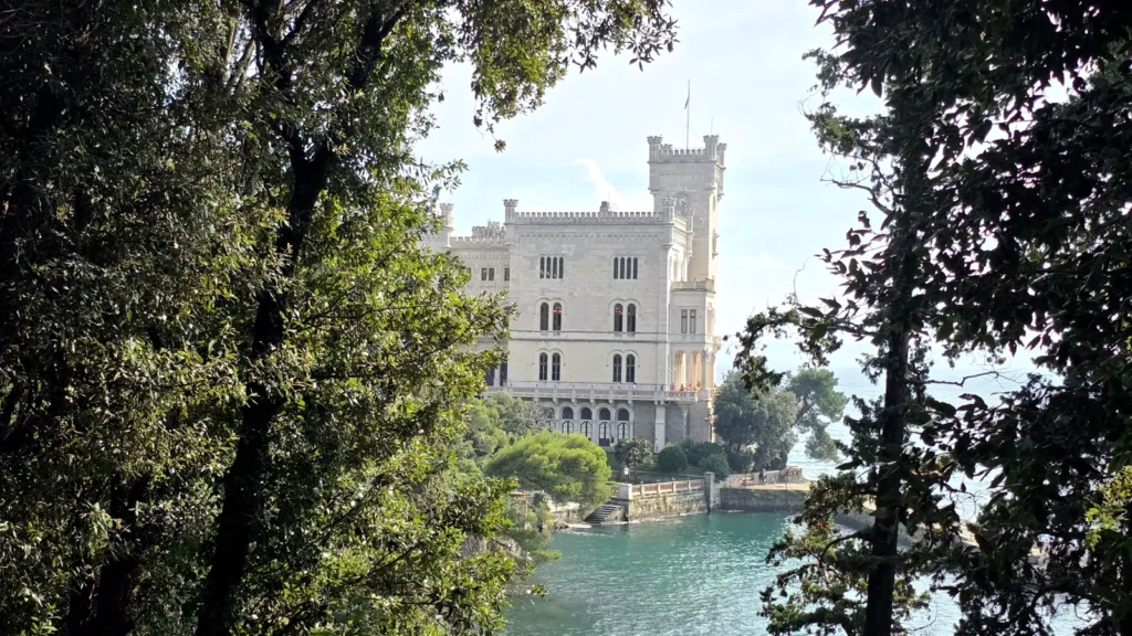 Castello bianco con torri incornicato da vegetazione verde, affacciato su acque turchesi.