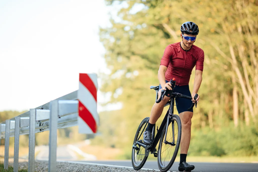Ciclista in maglia bordeaux affronta una curva segnalata su una strada circondata da boschi.