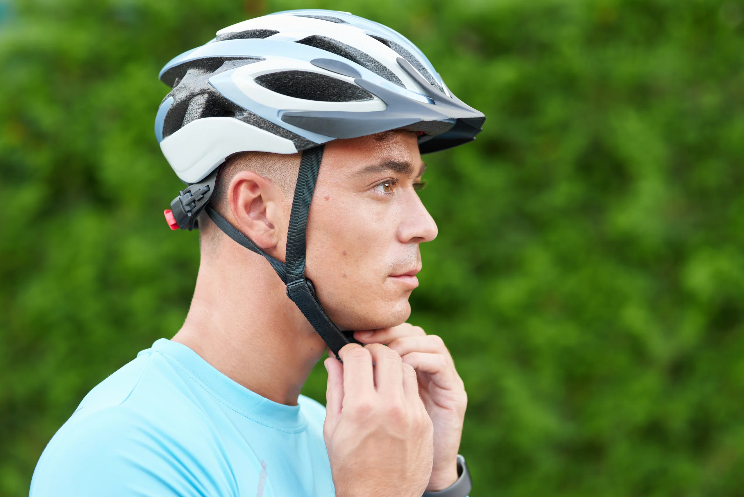 Ciclista che allaccia il casco bianco e nero prima di partire, con sfondo di vegetazione verde.