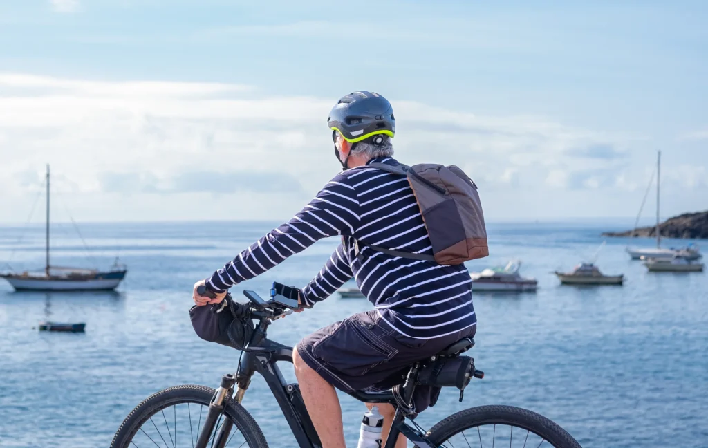 Ciclista con zaino e casco guida bicicletta davanti a baia con barche ormeggiate.