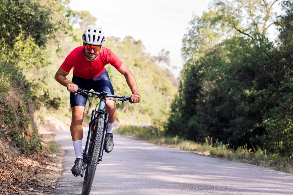 Ciclista in maglia rossa su strada sterrata circondata da vegetazione lussureggiante.