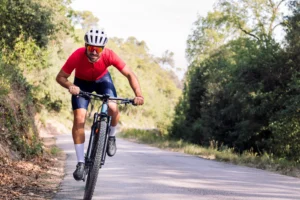Ciclista in maglia rossa su strada sterrata circondata da vegetazione lussureggiante.