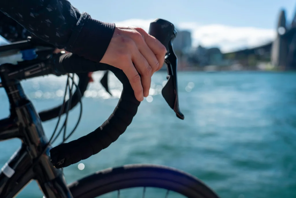 Mano su freno a leva di bicicletta, mare azzurro e costa sfocata sullo sfondo.