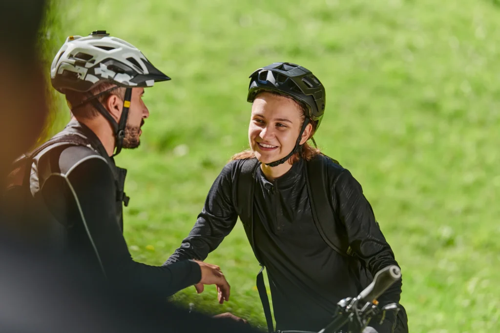 Due ciclisti si salutano su un sentiero con sfondo di prato verde brillante.