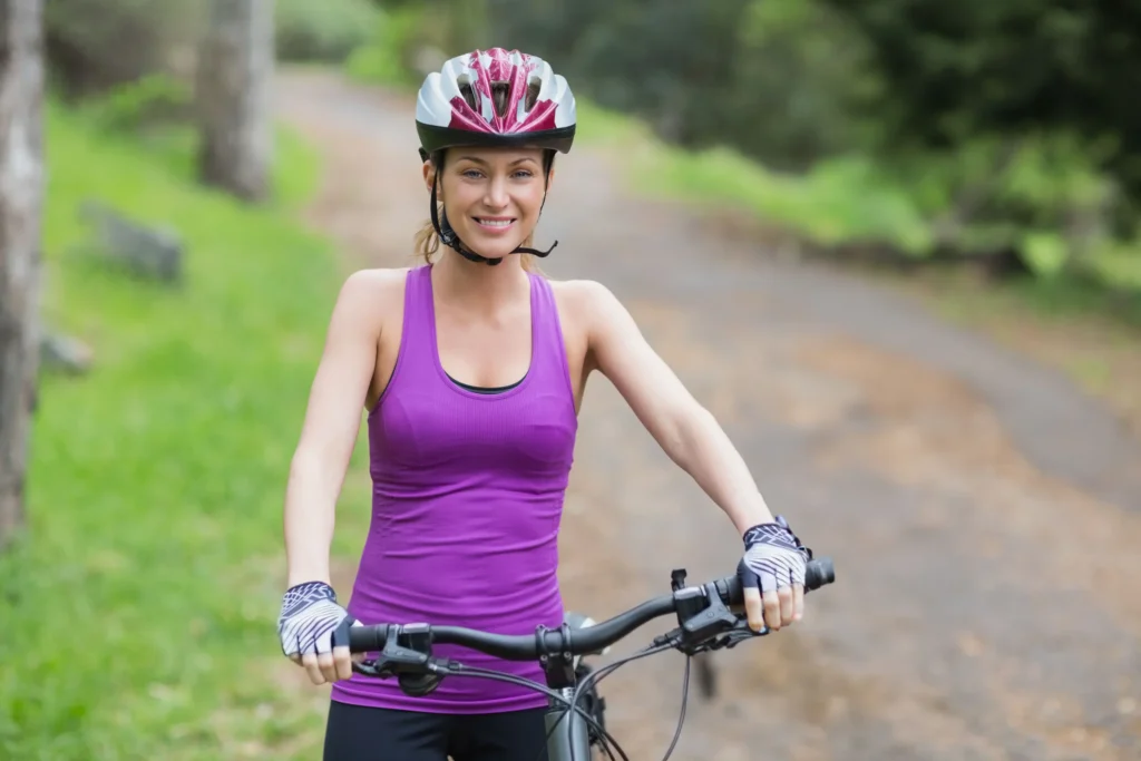 Ciclista con casco rosa e maglietta viola su sentiero di campagna circondato da verde.