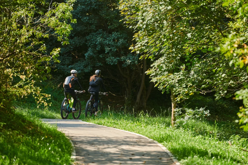 Due ciclisti su una ciclovia asfaltata immersa in vegetazione verde lussureggiante e alberi ad alto fusto.