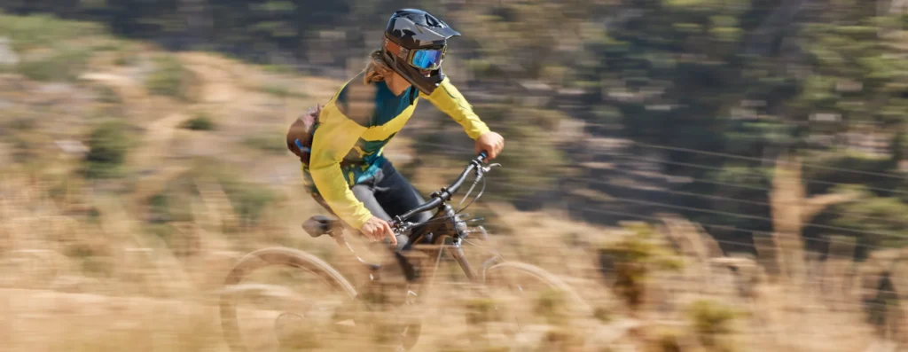 Bikers in giallo affronta un singletrail in salita su terreno sabbioso e accidentato.