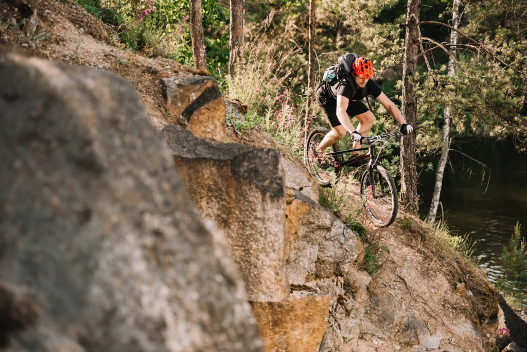 Ciclista con casco rosso affronta un sentiero sterrato in discesa tra rocce e alberi.