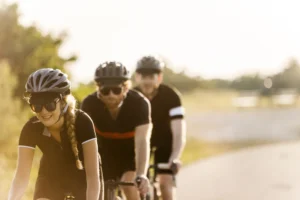 Tre cicloturisti pedalano su una ciclovia piatta lungo un corso d'acqua, con alberi e vegetazione sullo sfondo.